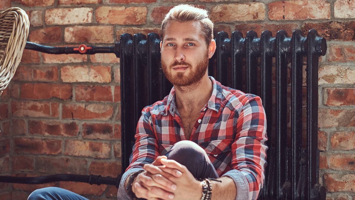Male creator in a plaid shirt sitting against a brick wall
