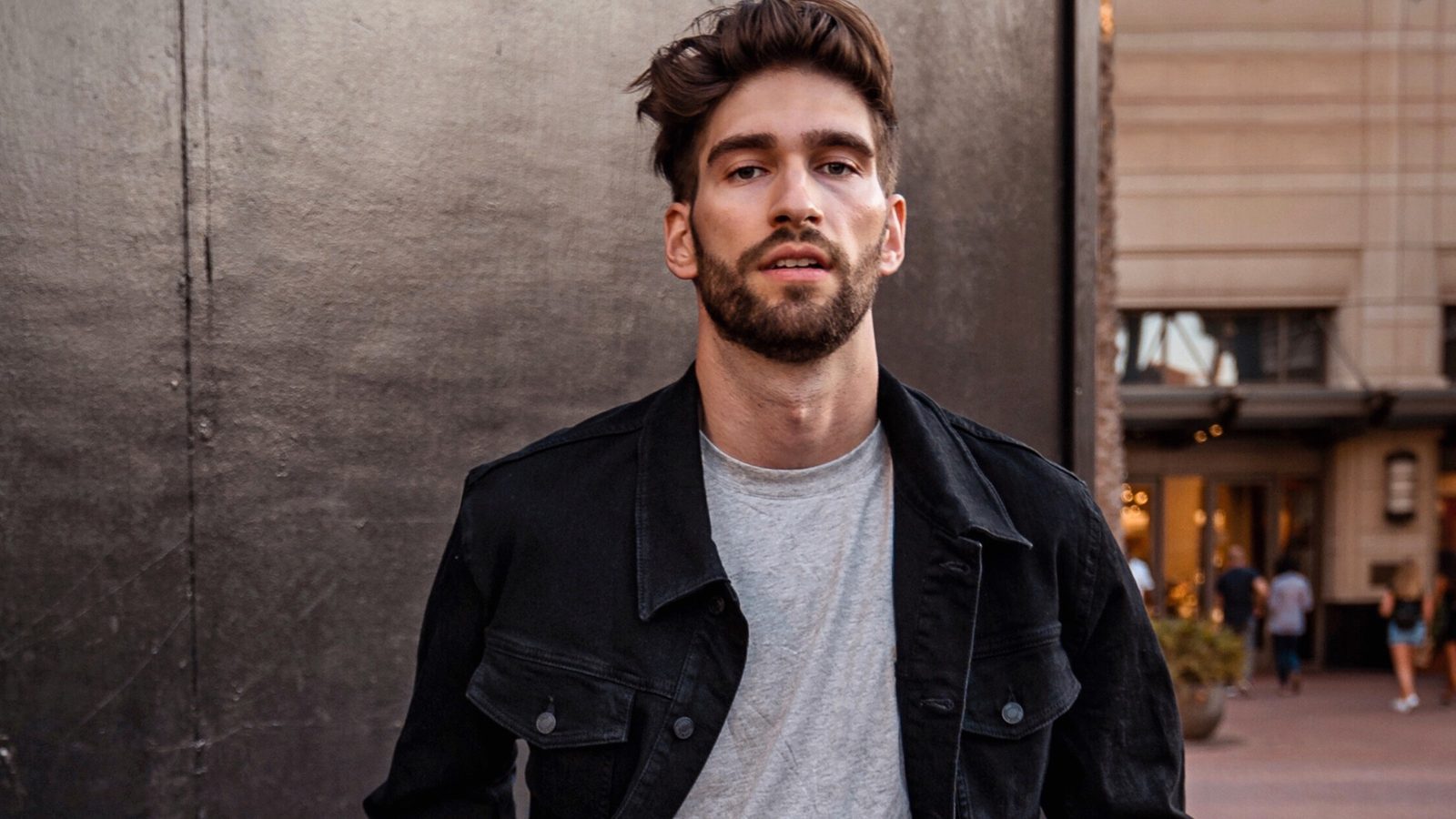 Bearded male creator in a black denim jacket standing on a city street